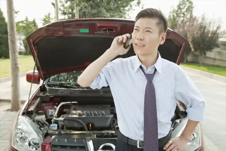 Driver calling for roadside assistance beside a broken-down car